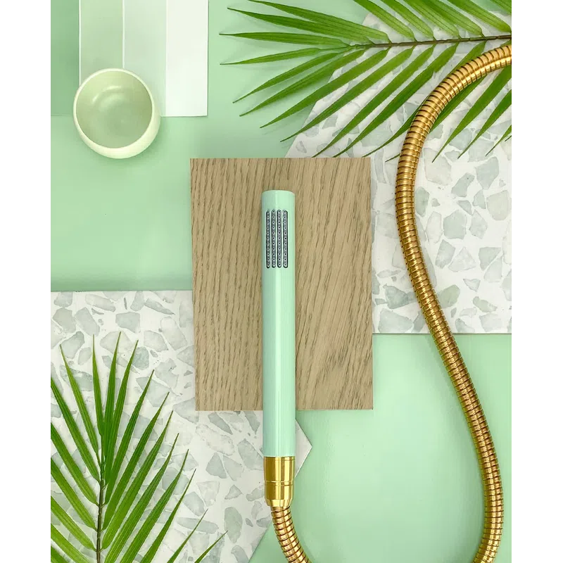 Mint green handheld shower head with gold hose on wood and terrazzo surfaces with green leaves