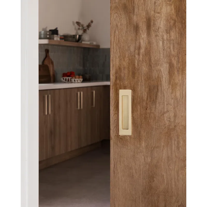 Sliding wooden door with recessed handle partially open to reveal modern kitchen with wooden cabinets and countertop.