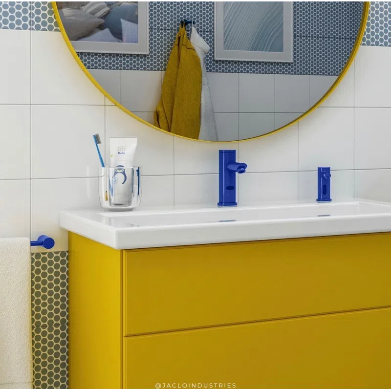 Modern bathroom sink with yellow vanity, blue faucet, round mirror, and hexagonal tile backsplash.