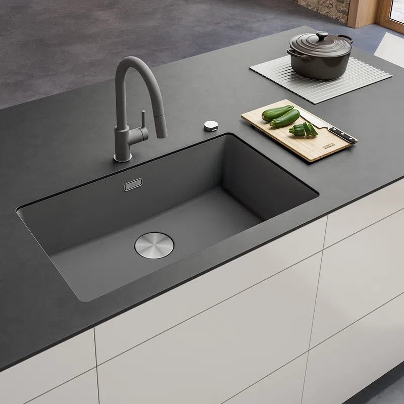 Modern kitchen sink with matte black faucet on dark countertop, cutting board with zucchini, and pot in background