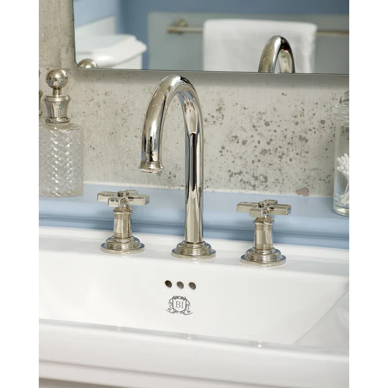 Chrome bathroom faucet with cross handles above white sink and decorative glass containers on sides