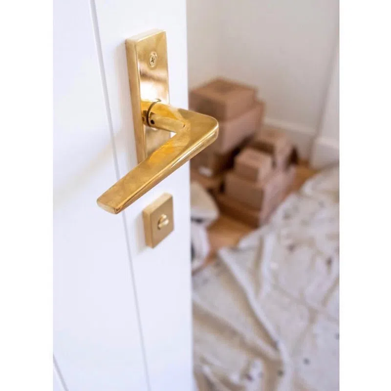 Close-up of a gold door handle on a white door with stacked cardboard boxes and a drop cloth in the background