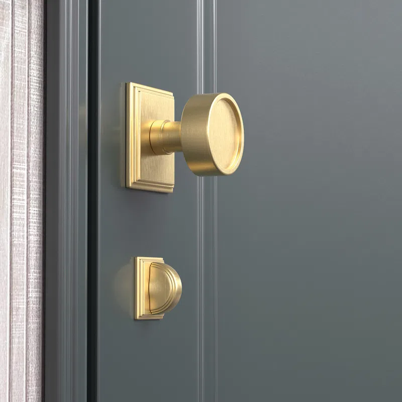 Elegant gold door knob and lock set on a dark gray paneled door with a textured curtain edge visible.