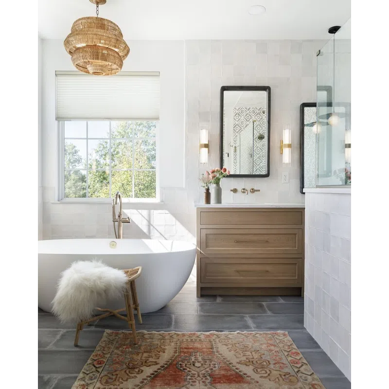 Bright modern bathroom with freestanding tub, wooden vanity, rattan stool with fur, and patterned rug.