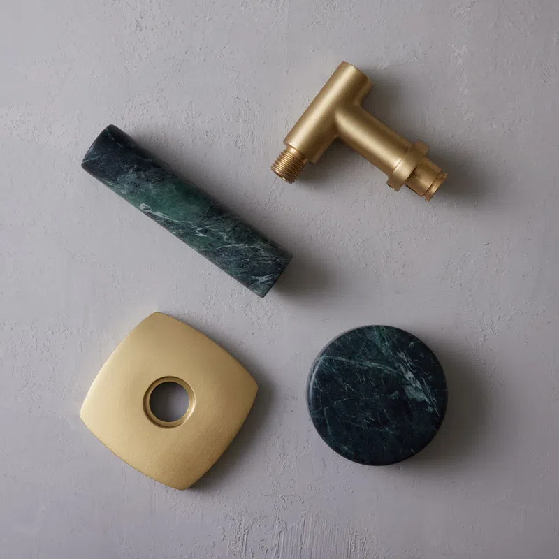 Brass faucet parts and green marble accessories displayed on a textured gray surface.