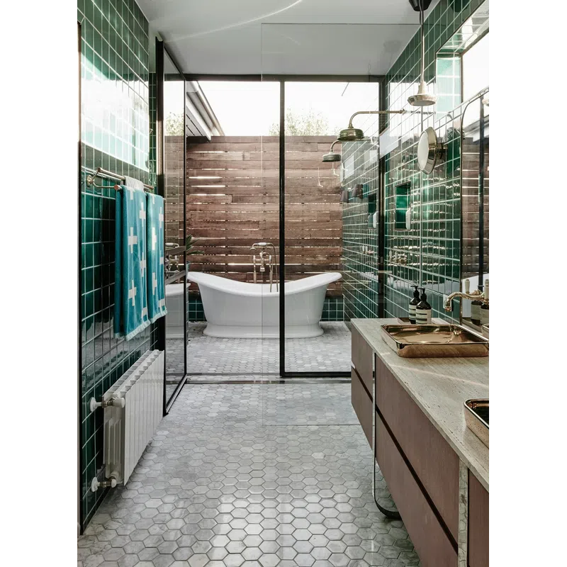 Modern bathroom with green tiles, hexagonal floor, freestanding tub, glass shower, and wooden vanity with gold fixtures.