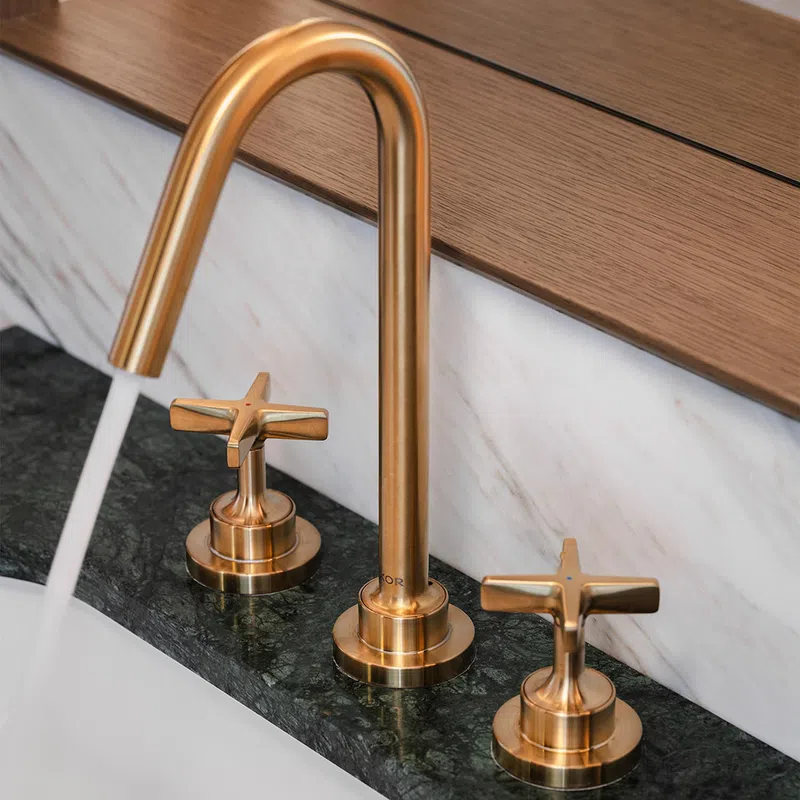 Modern gold faucet with running water on dark green marble countertop and wooden backsplash.