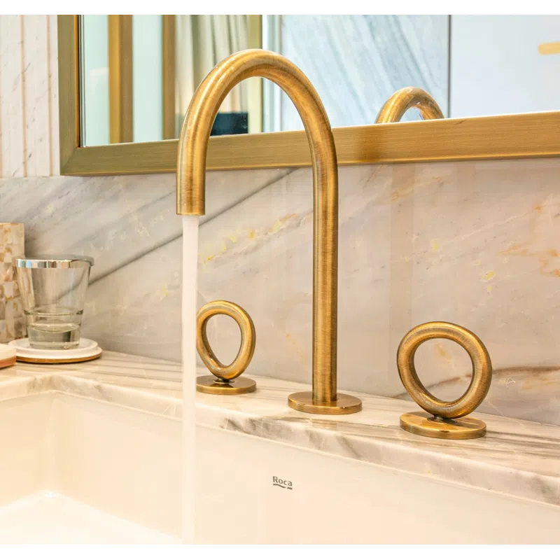 Modern gold bathroom faucet with circular handles on marble countertop and running water in a white sink.