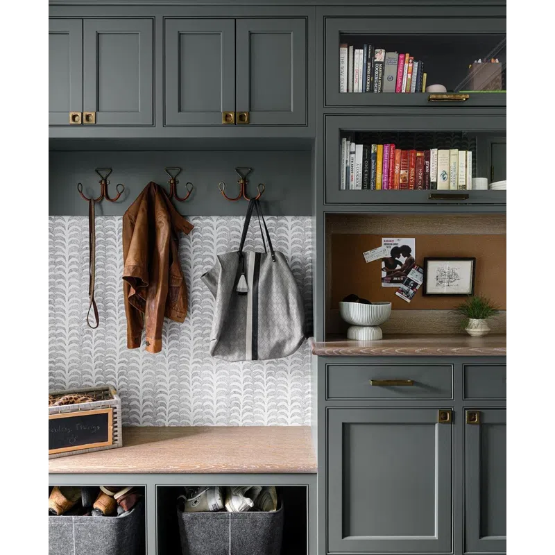 Organized mudroom with gray cabinets, wooden bench, coat hooks, handbags, books, and storage bins below bench.