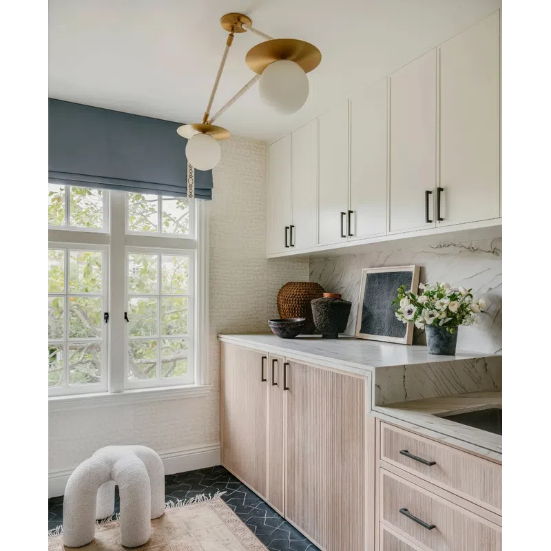 Bright kitchen corner with white and wood cabinets, marble countertop, modern light fixture, and decorative plants.