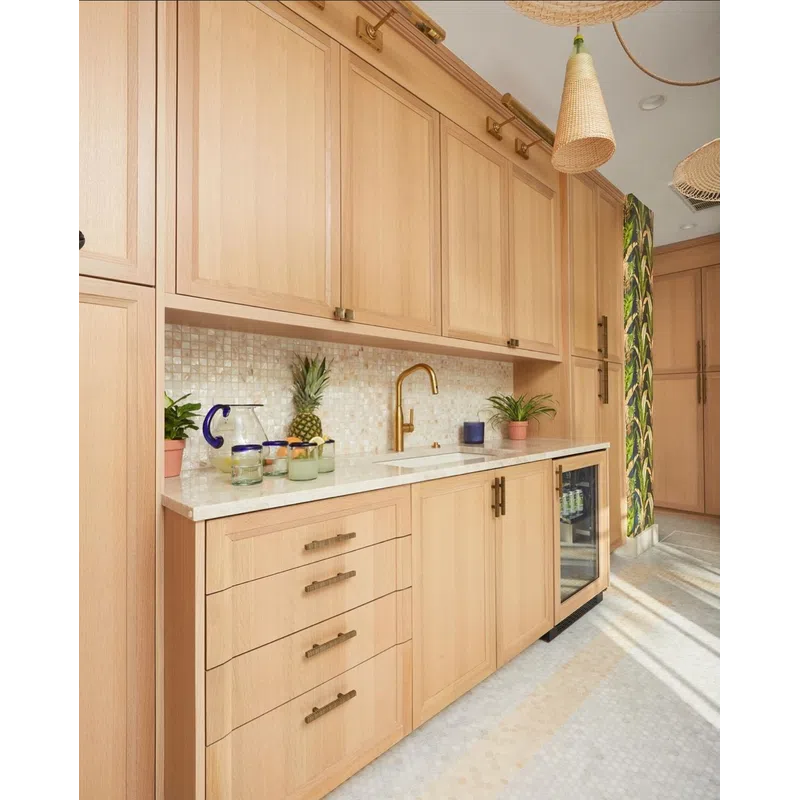 Light wood kitchen cabinets with gold faucet, mosaic tile backsplash, and tropical-themed wallpaper accent.