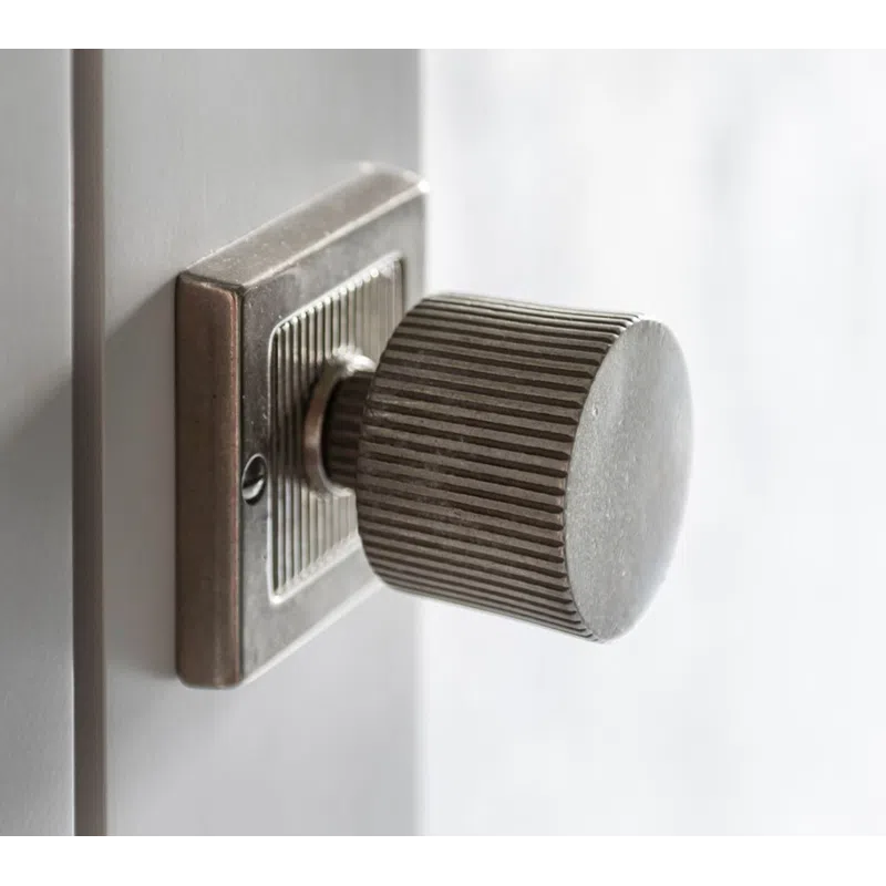 Close-up of a vintage metal door knob with ridged texture on a white wooden door.