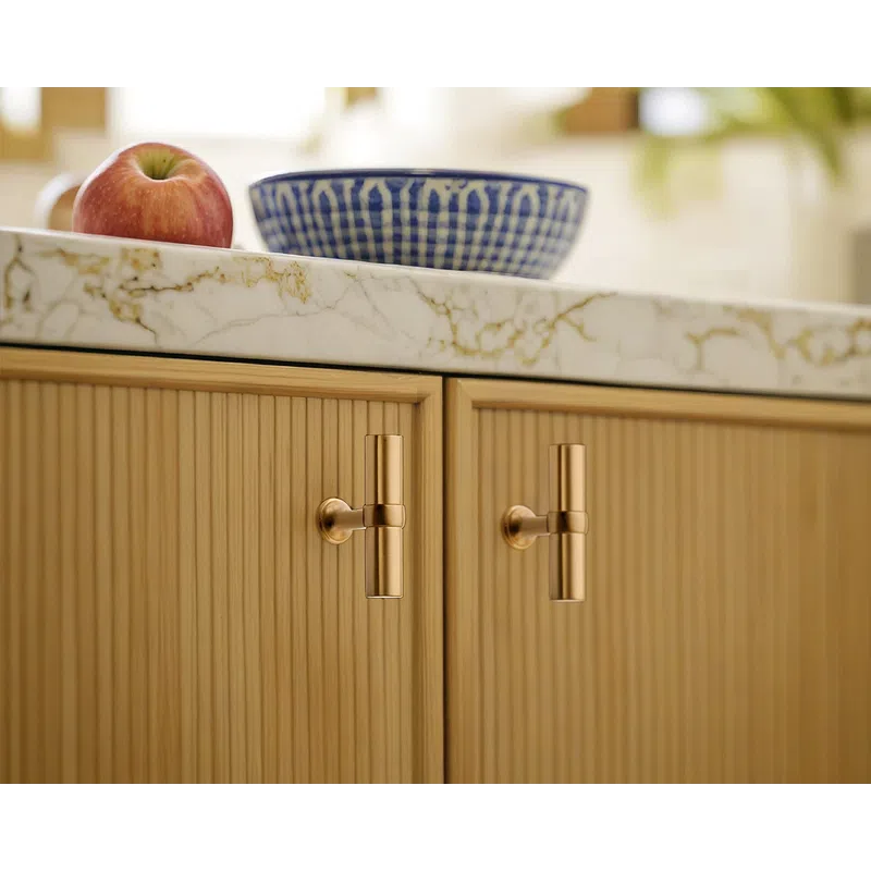 Brass cabinet handles on wood grain kitchen cabinets with marble countertop holding a red apple and blue bowl