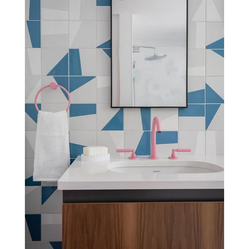 Modern bathroom sink with pink faucet and towel ring, geometric blue and white tiled wall, and wooden cabinet.