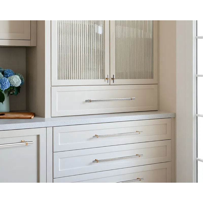Modern white kitchen cabinets with ribbed glass doors and sleek metallic handles beside a bouquet of blue and white flowers.