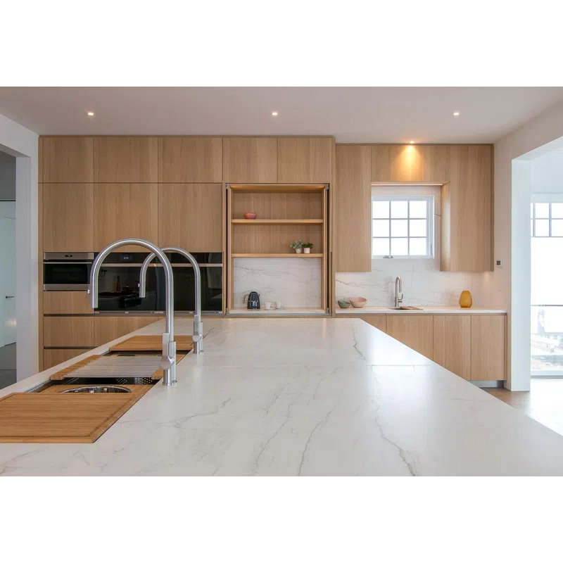 Modern kitchen with expansive marble island, light wood cabinetry, dual sink faucets, and built-in oven