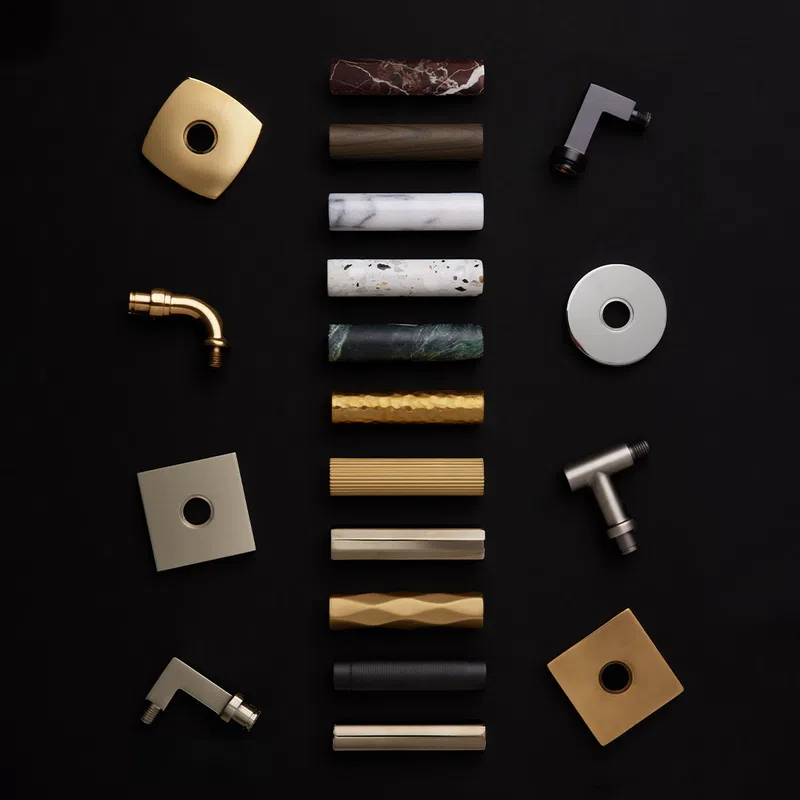Various cylindrical and square faucet handles and parts in gold, marble, wood, and metal finishes on black.