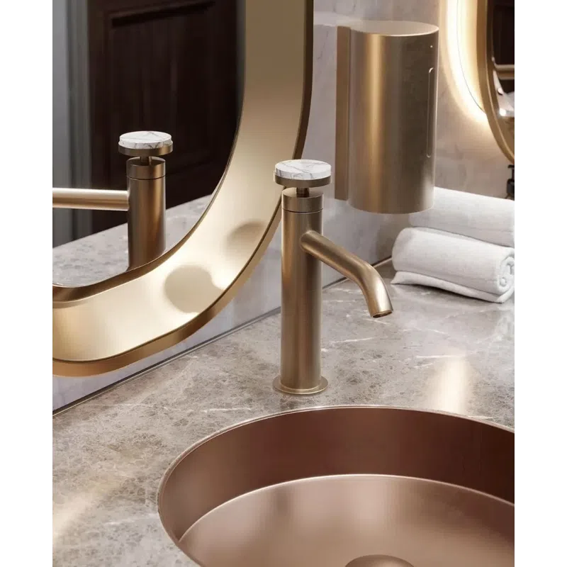 Modern gold faucet and round sink on marble countertop with mirror and rolled white towels in bathroom.