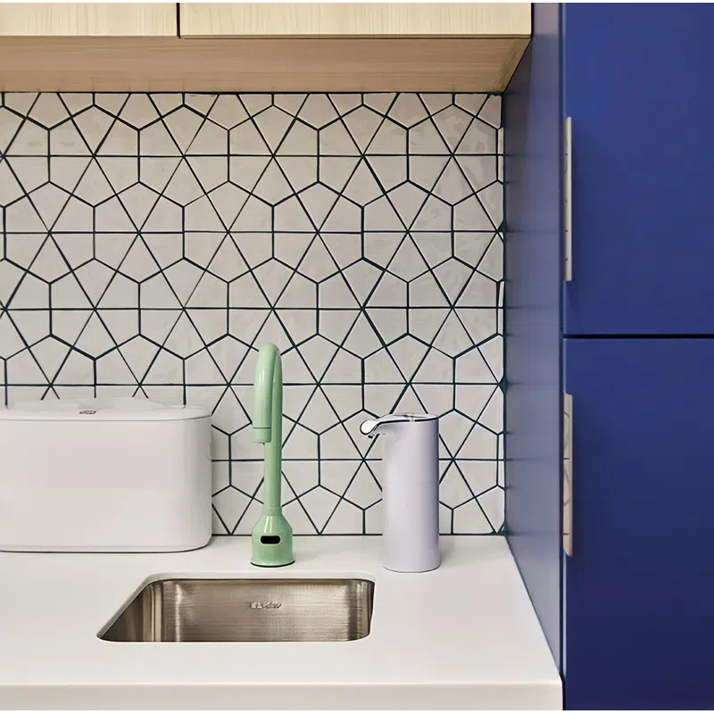 Modern kitchen sink area with geometric tile backsplash, green faucet, white dispenser, and blue cabinets.