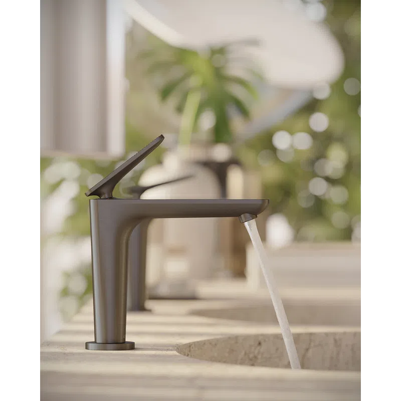 Modern matte black faucet releasing water over a stone sink with blurred green plant background.