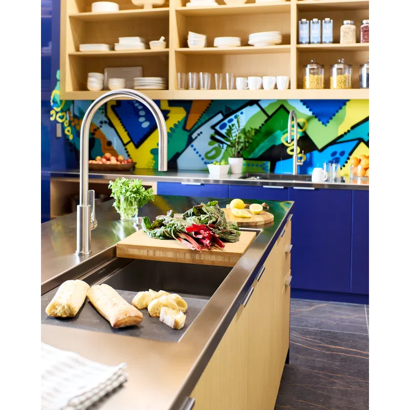Modern kitchen with stainless steel sink, fresh vegetables, bread, colorful backsplash, and wooden shelves.