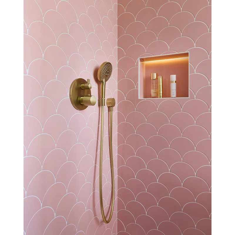 Modern shower with gold fixtures and pink scalloped wall tiles featuring a built-in illuminated niche with toiletries.