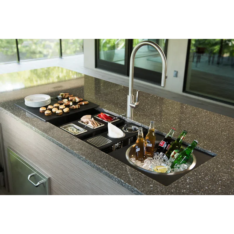 Outdoor kitchen countertop with built-in sink, ice bucket with drinks, appetizers, and modern faucet under natural light.