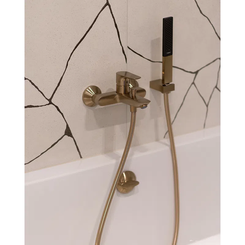 Modern gold bathtub faucet and hand shower against white wall with black abstract lines in a bathroom.