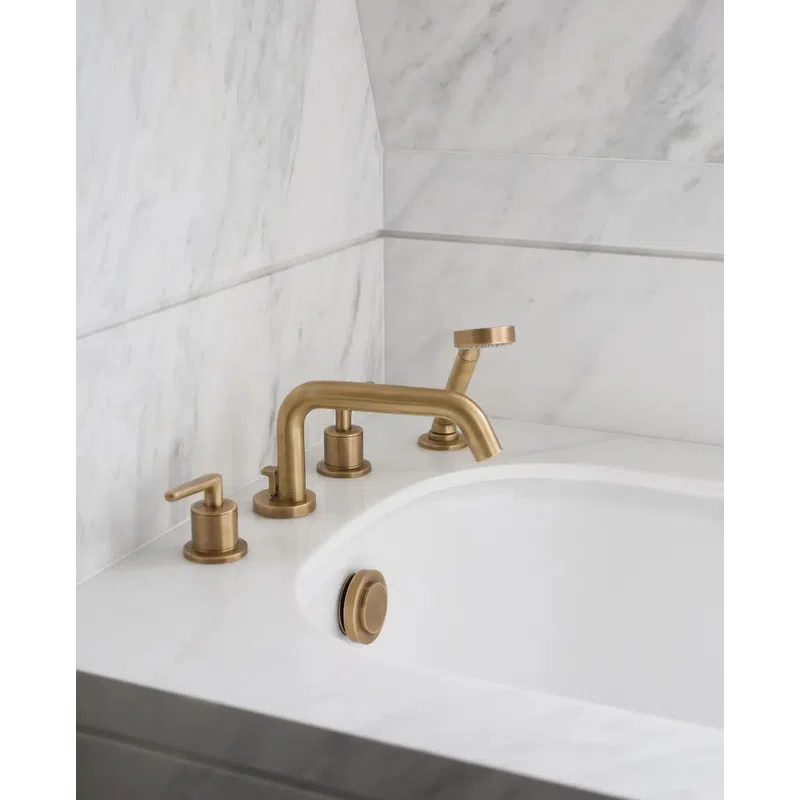 Modern bathtub with brushed gold faucet and handheld shower on white marble countertop and wall.