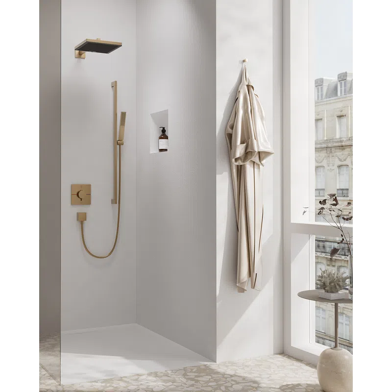 Minimalist bathroom shower with gold fixtures, beige robe, terrazzo floor, and large window overlooking city buildings.