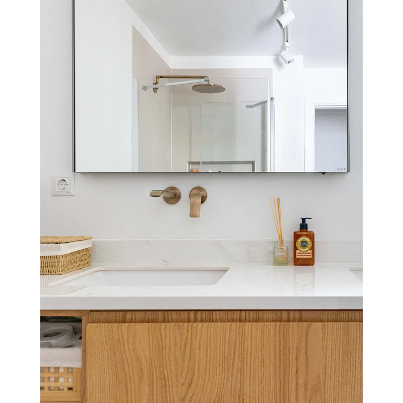 Modern bathroom sink with brushed brass faucet, large mirror, wooden vanity, and toiletry accessories on countertop