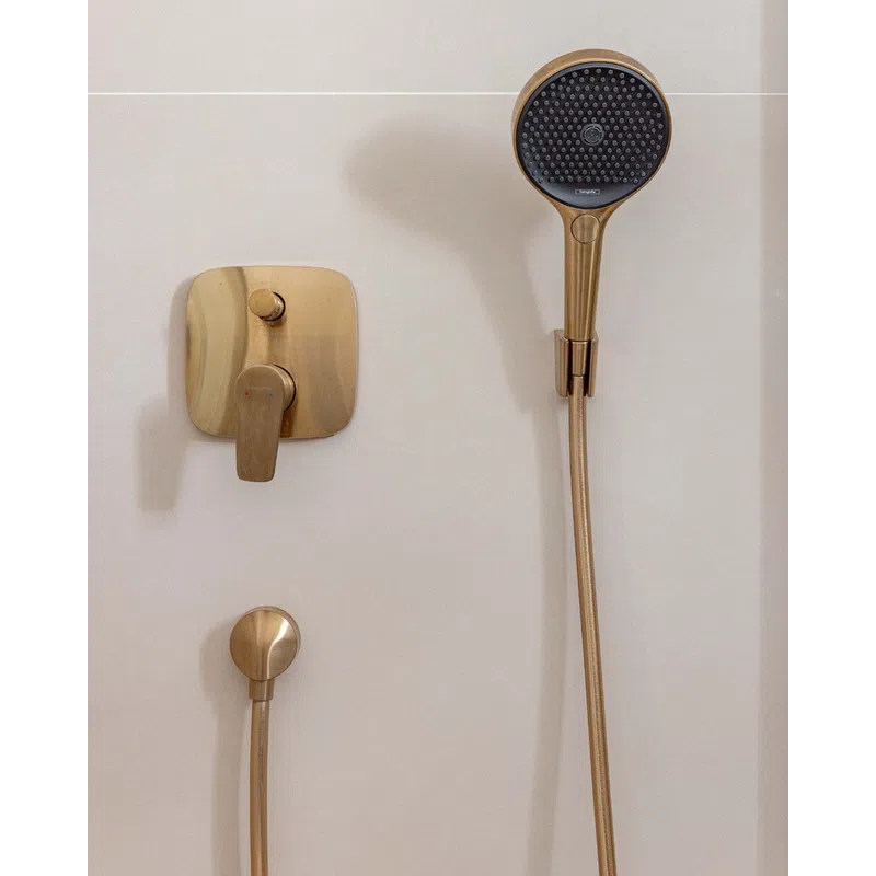 Modern gold showerhead and matching control knobs mounted on a clean white bathroom wall.