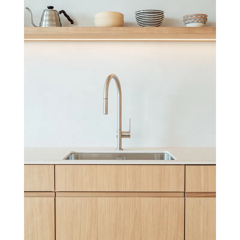 Minimalist kitchen sink with stainless steel faucet, light wood cabinets, and decorative bowls on shelf above.