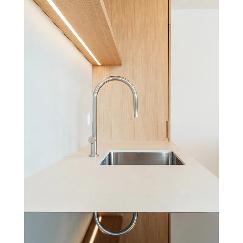 Modern kitchen sink with stainless steel faucet and wooden wall paneling under soft lighting