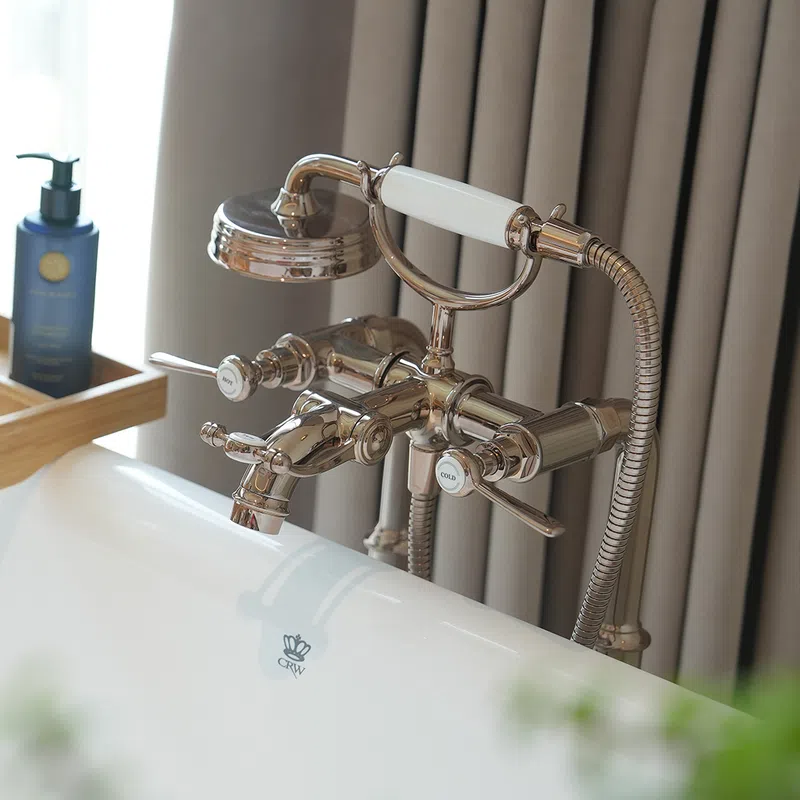 Chrome vintage-style bathtub faucet with handheld shower head mounted on white tub in modern bathroom.