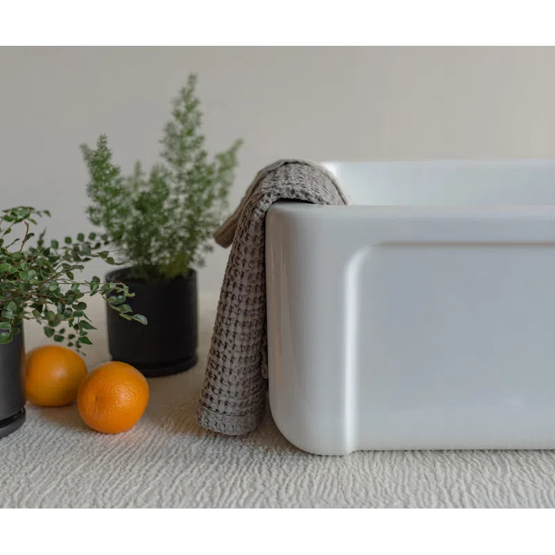 Whites ceramic sink with grey towel draped over edge, oranges, and potted green plants on textured surface.