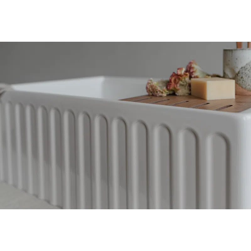 Modern white ceramic sink with ribbed sides featuring a wooden tray holding soap and dried flowers.