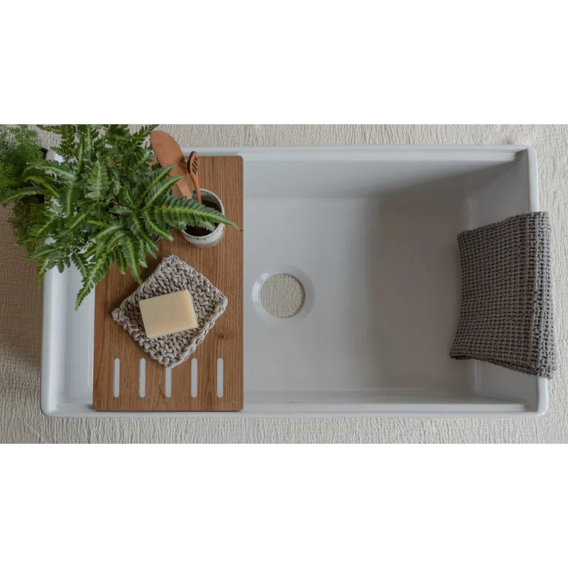Minimalist white bathtub with wooden tray holding soap, toothbrush, and green plant, plus gray towel on tub edge.