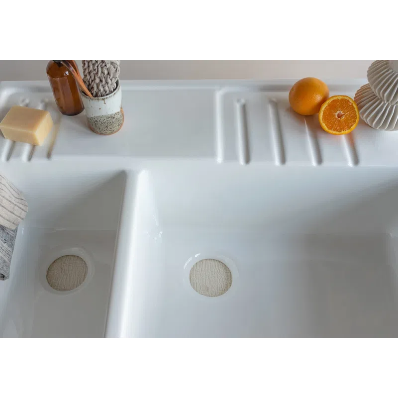 White double kitchen sink with a bar of soap, brown bottle, knitted cloth, and fresh oranges on the countertop.
