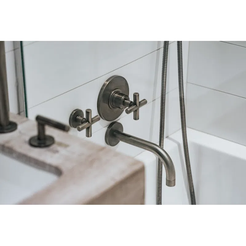 Matte black wall-mounted faucet and handles over a white bathtub with tile backsplash and stone countertop.