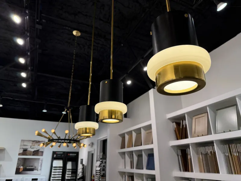 Modern pendant lights with gold and black design hanging from ceiling in a showroom with samples on shelves.