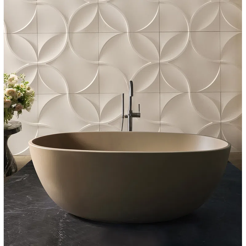Modern beige freestanding bathtub with geometric 3D wall tiles and floral arrangement on side table.