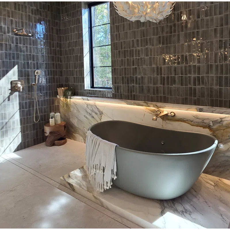 Modern bathroom with dark gray tiled walls, freestanding gray tub, marble accents, and leaf-shaped chandelier.
