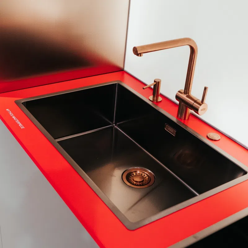 Modern black kitchen sink with copper faucet and soap dispenser set in vibrant red countertop.