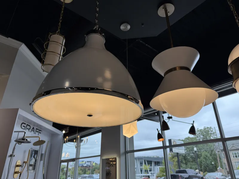 Modern pendant lights hanging from a dark ceiling in a showroom with large windows and outdoor view
