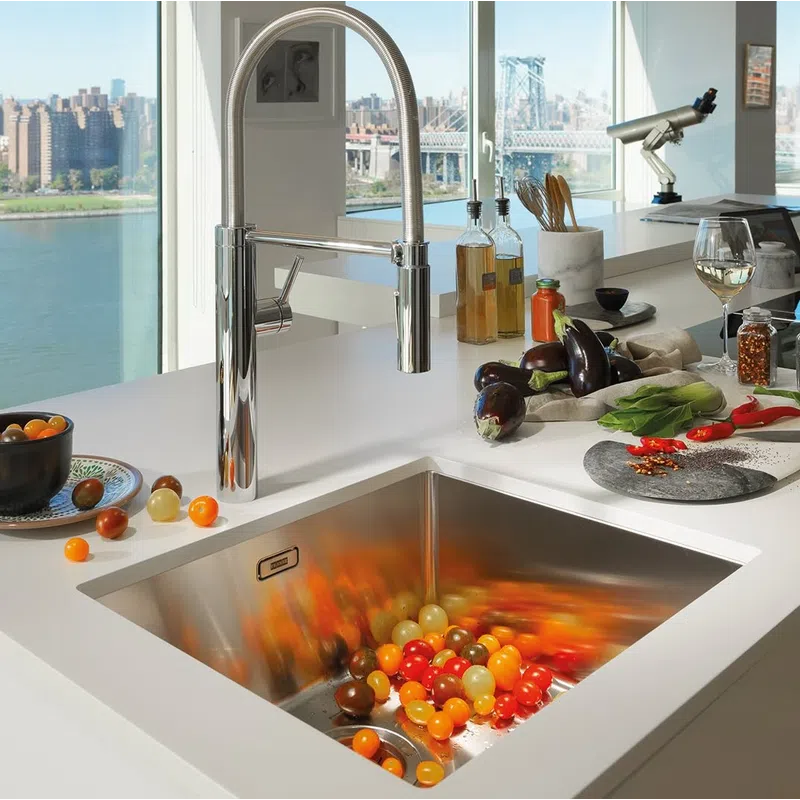 Modern kitchen sink with a chrome faucet, colorful tomatoes, eggplants, and city river view in the background