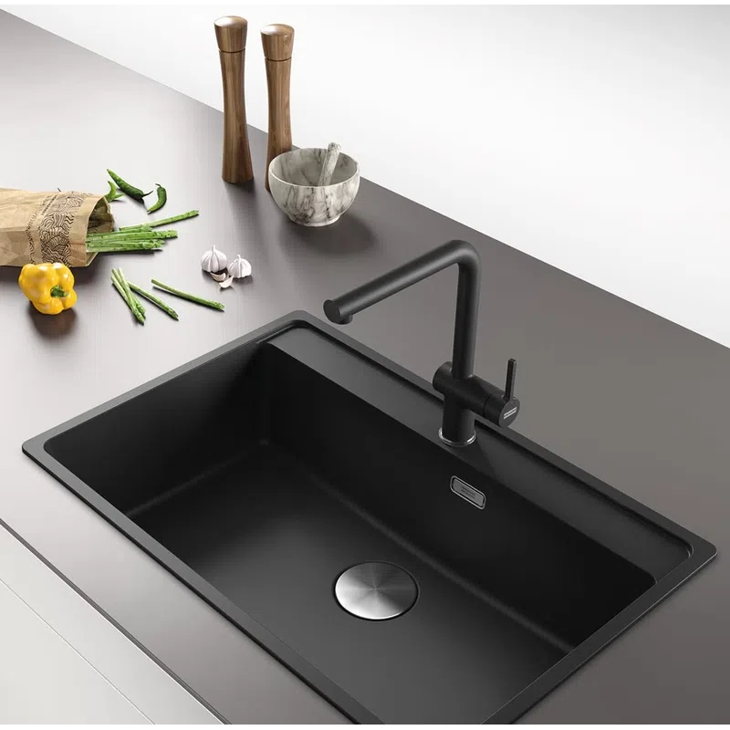 Modern black kitchen sink with matte black faucet on gray countertop with vegetables and kitchen tools nearby