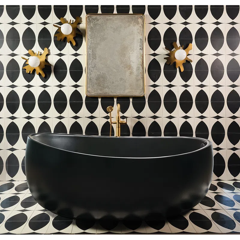 Modern black freestanding bathtub with gold faucet against black and white geometric tiled wall with decorative lights.