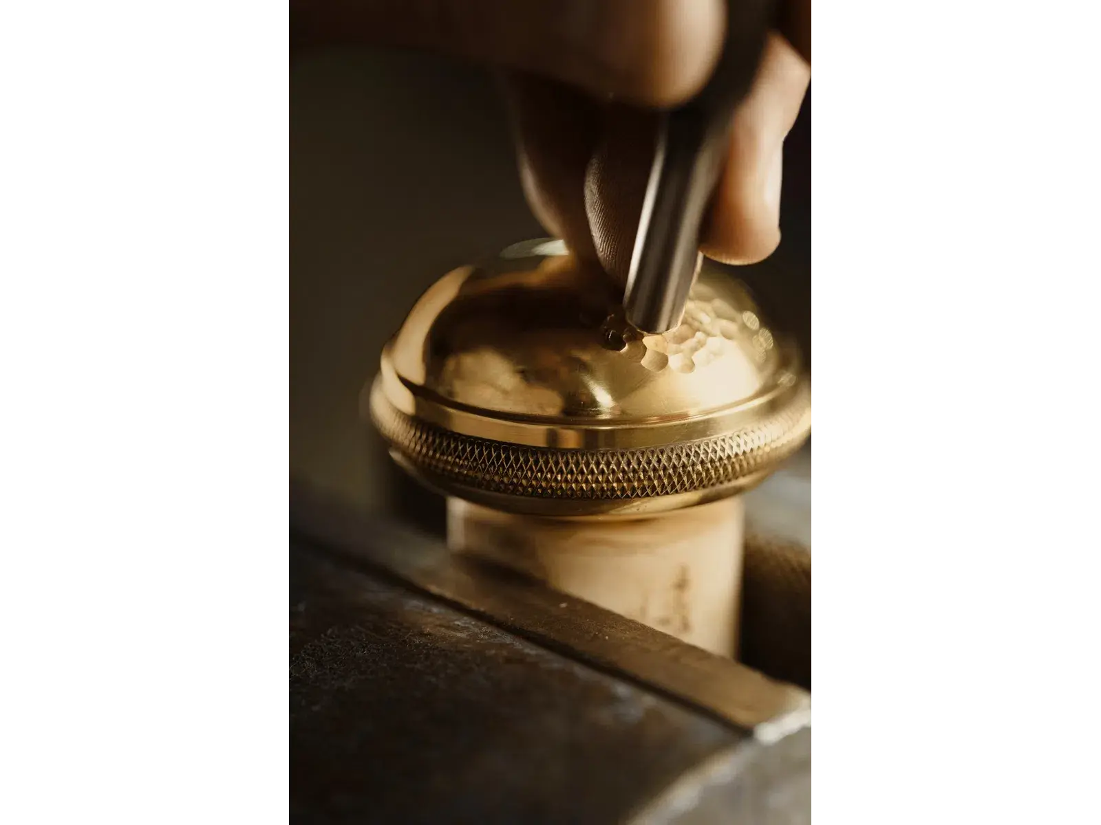 Close-up of hand engraving intricate patterns onto a shiny golden metal surface with engraving tool.