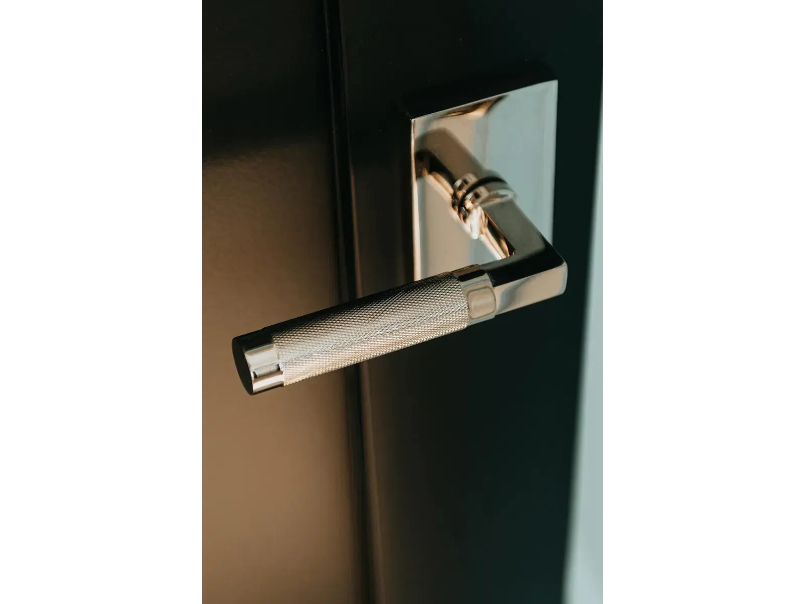 Close-up of a modern textured silver door handle on a black door with a reflective metal base plate.